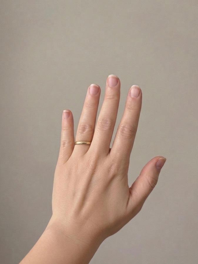 A bare hand with short natural nails, photographed against a plain wall