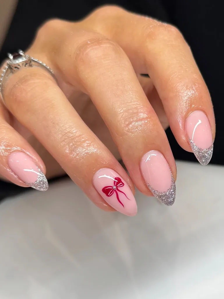 pink christmas nails with silver glitter tips and red bow accent