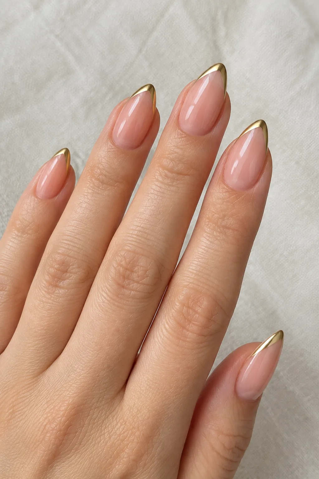 Short almond nails in sheer peach with slim diagonal gold french tips that make short fingers look longer