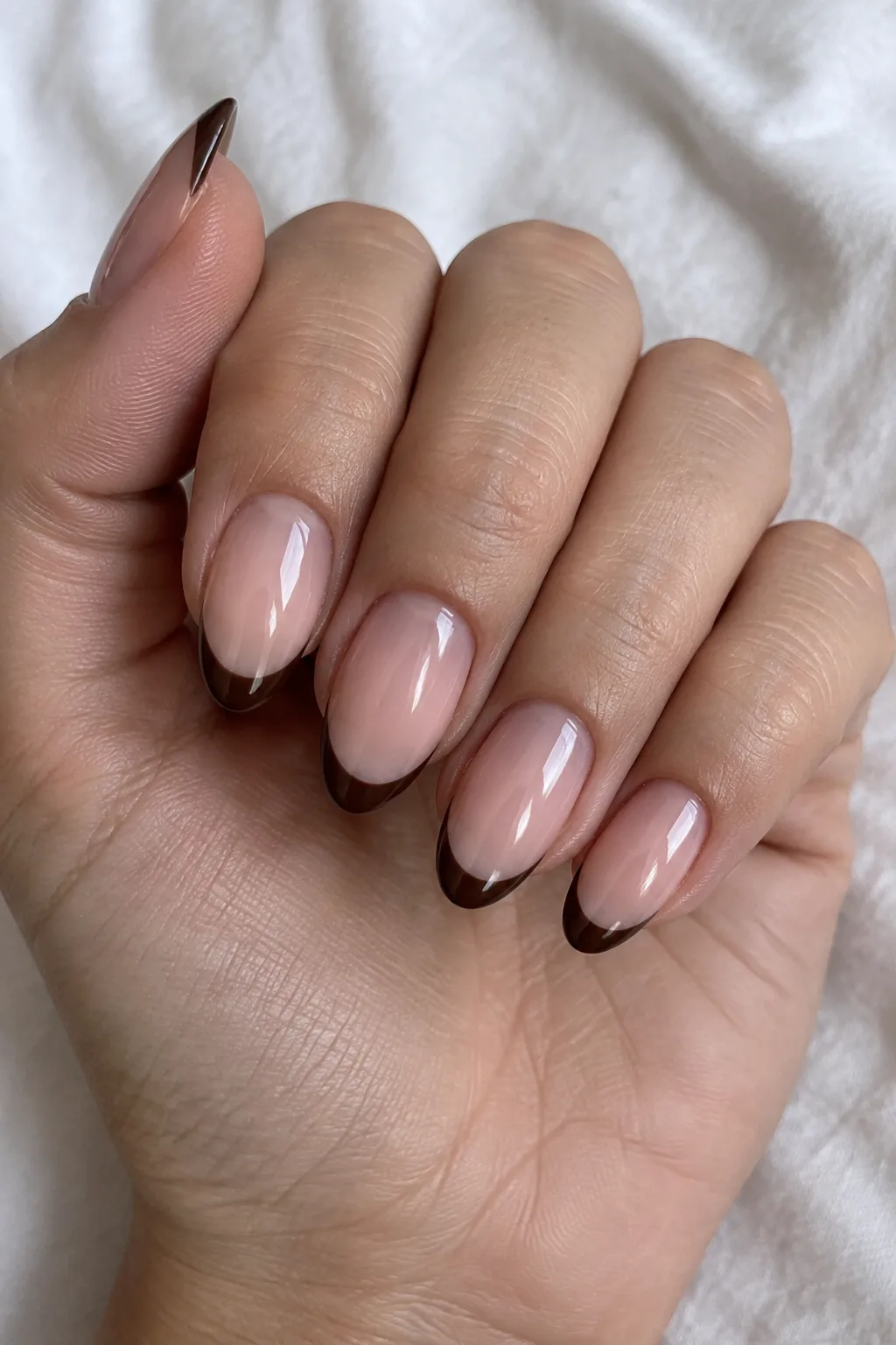 Nude almond nails topped with crisp chocolate brown French tip lines