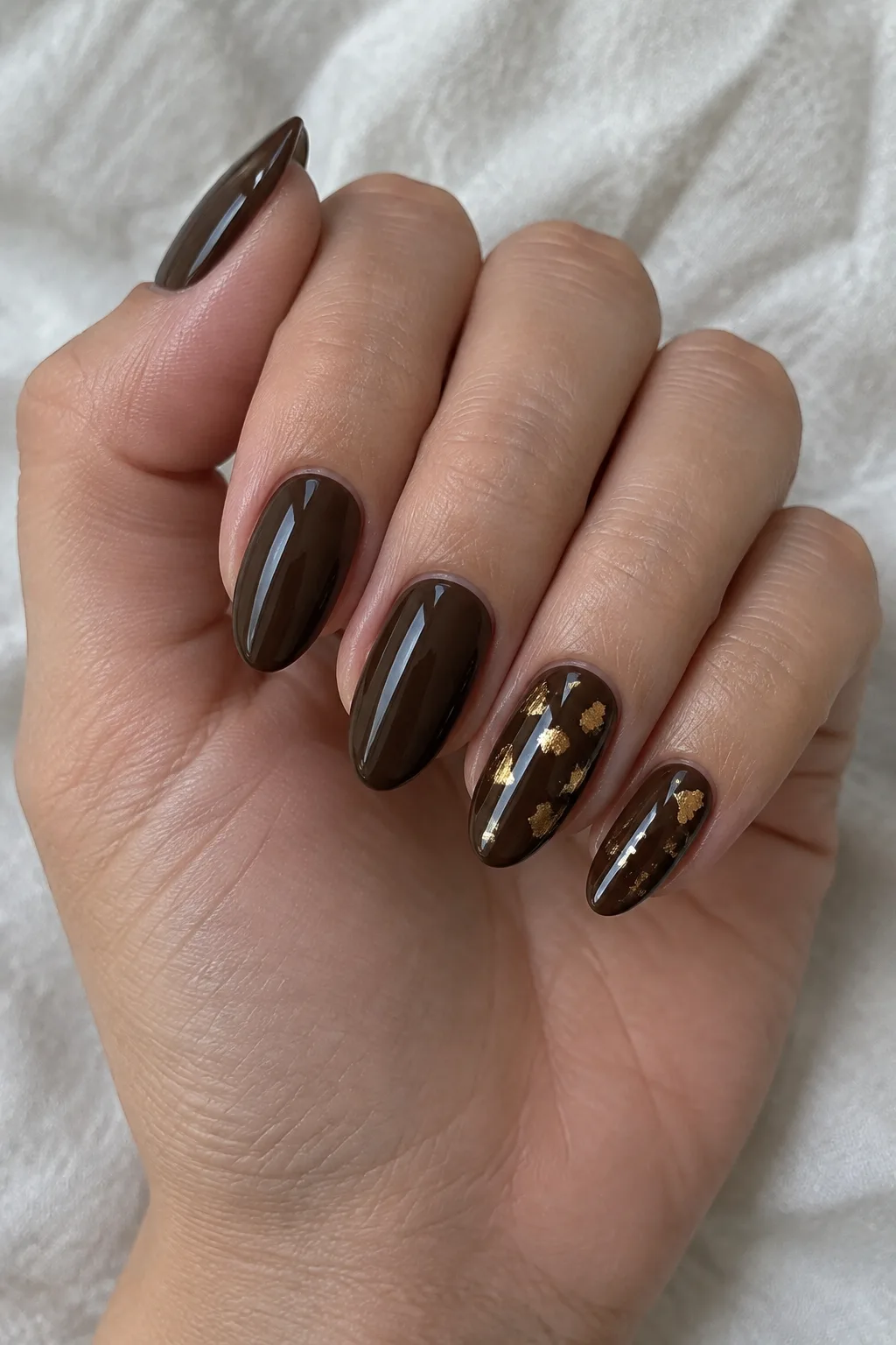 Espresso almond nails with scattered gold foil flecks on accent fingers