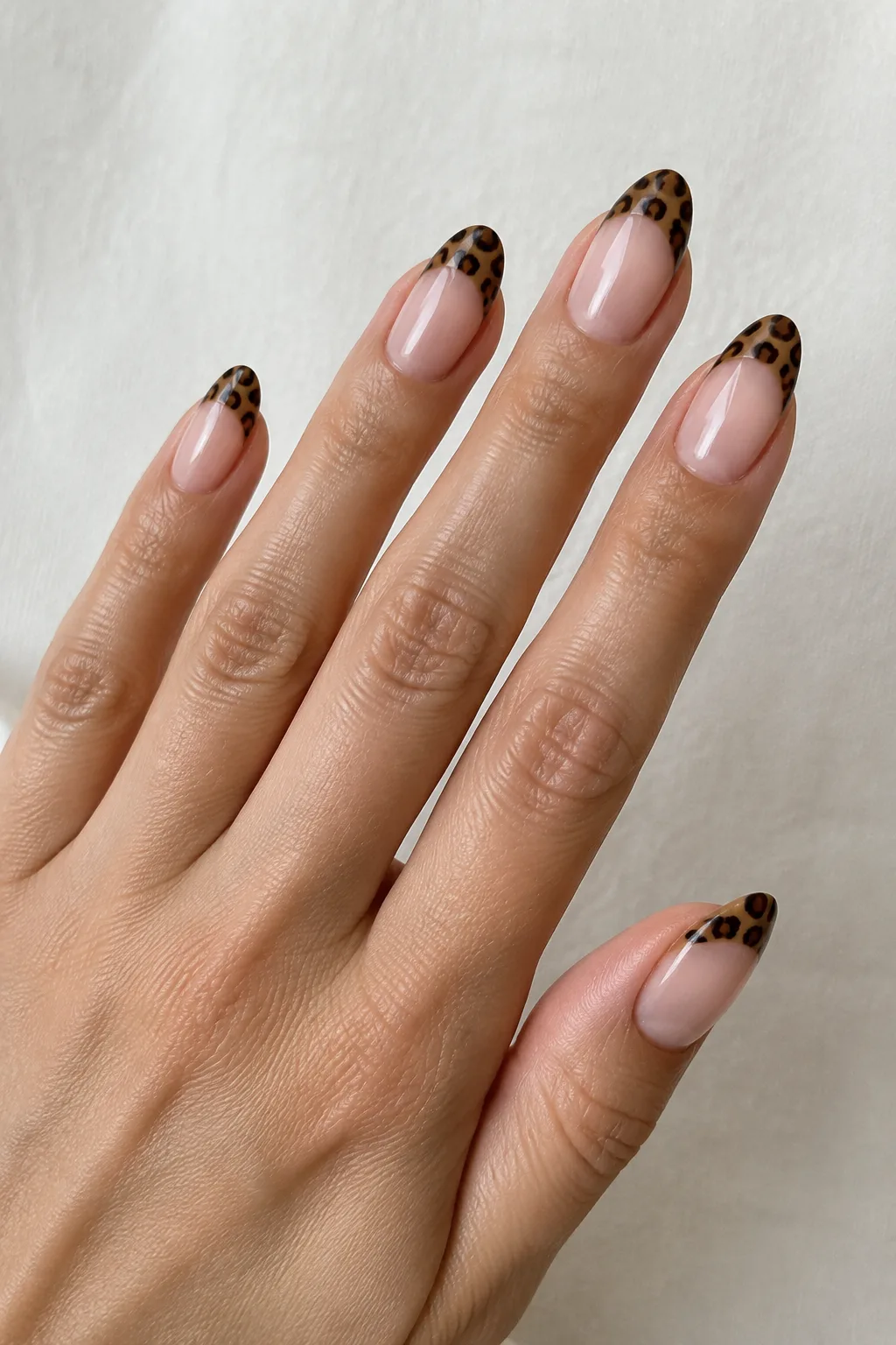Leopard print painted inside a nude French tip on medium oval nails