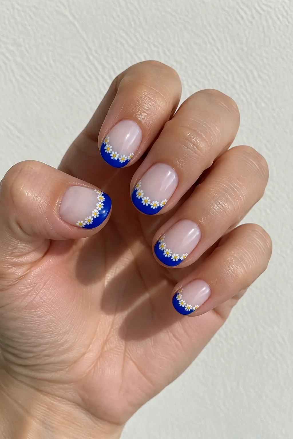 Tiny daisy flowers painted along the smile line on short round nails