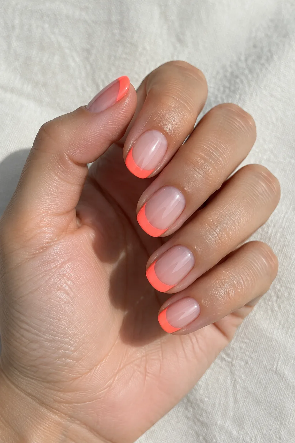 Neon coral French tips on short round nails with a glossy summer finish