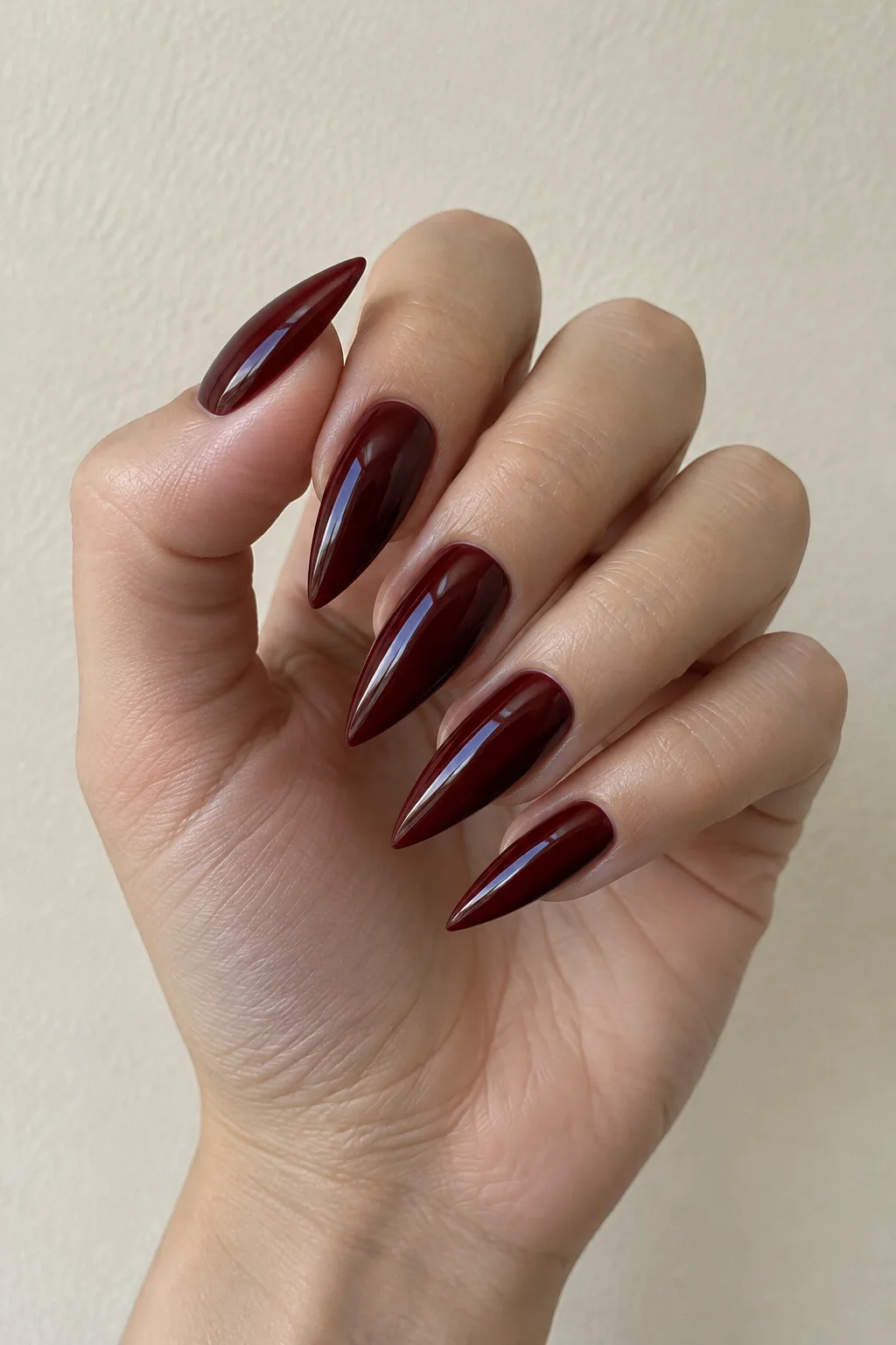 Oxblood red nails with a geometric arrowhead design near the cuticle line
