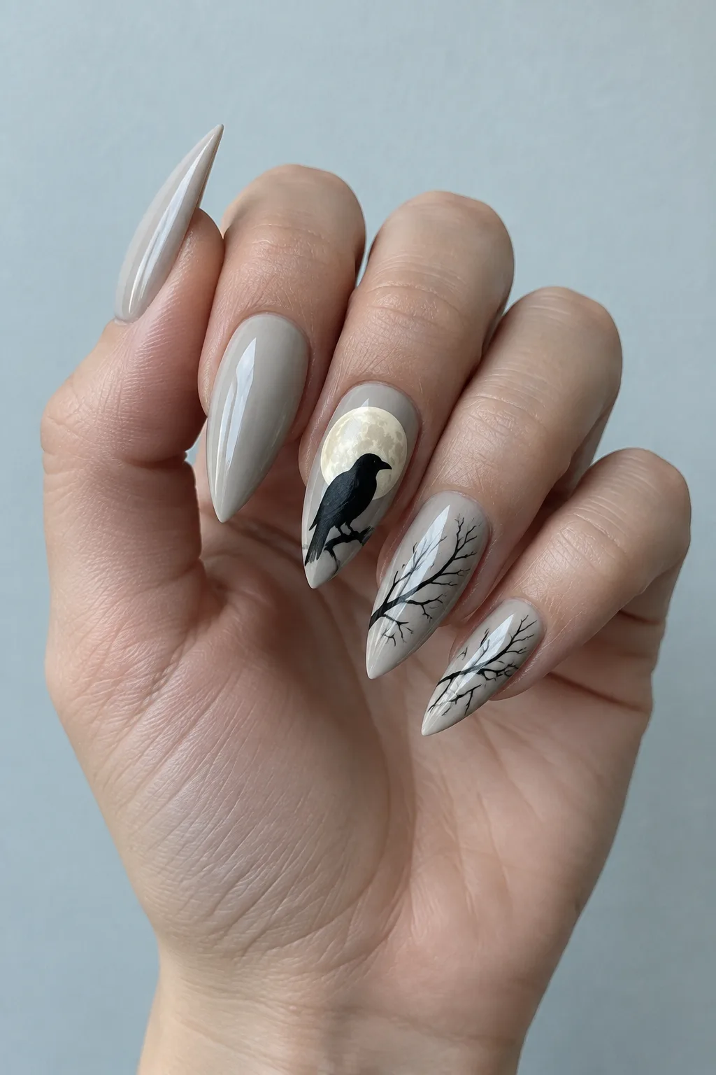 Pale bone gray stiletto nails with a raven silhouette against a full moon