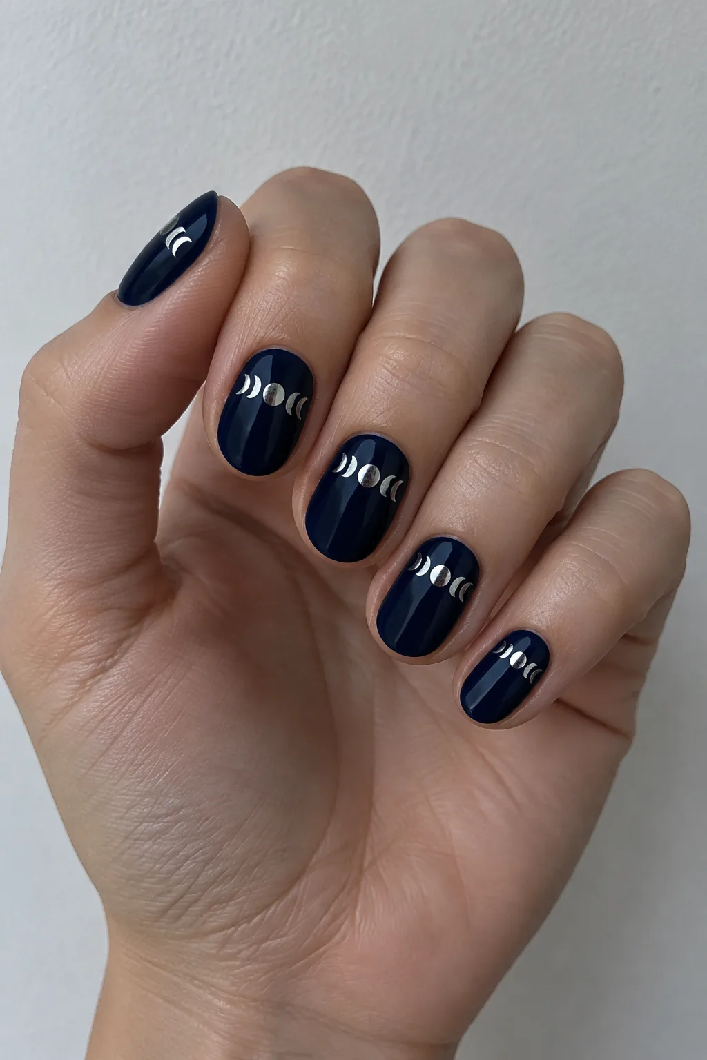 Deep navy short oval nails with silver moon phase illustrations