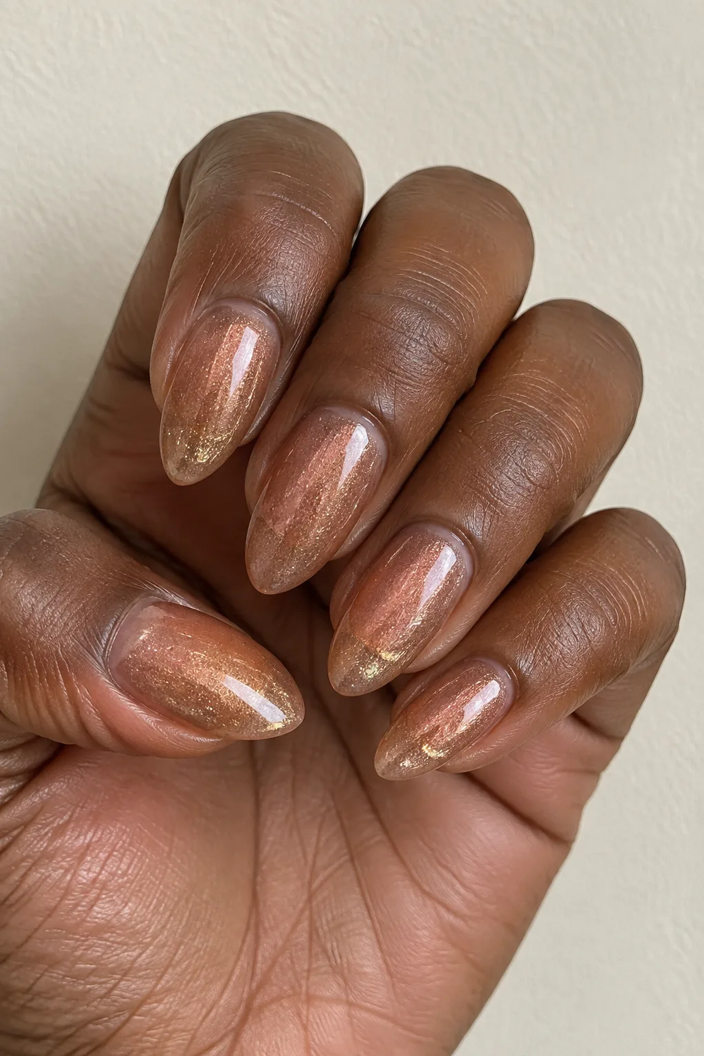 Sheer bronze shimmer polish on almond-shaped nails catching the light