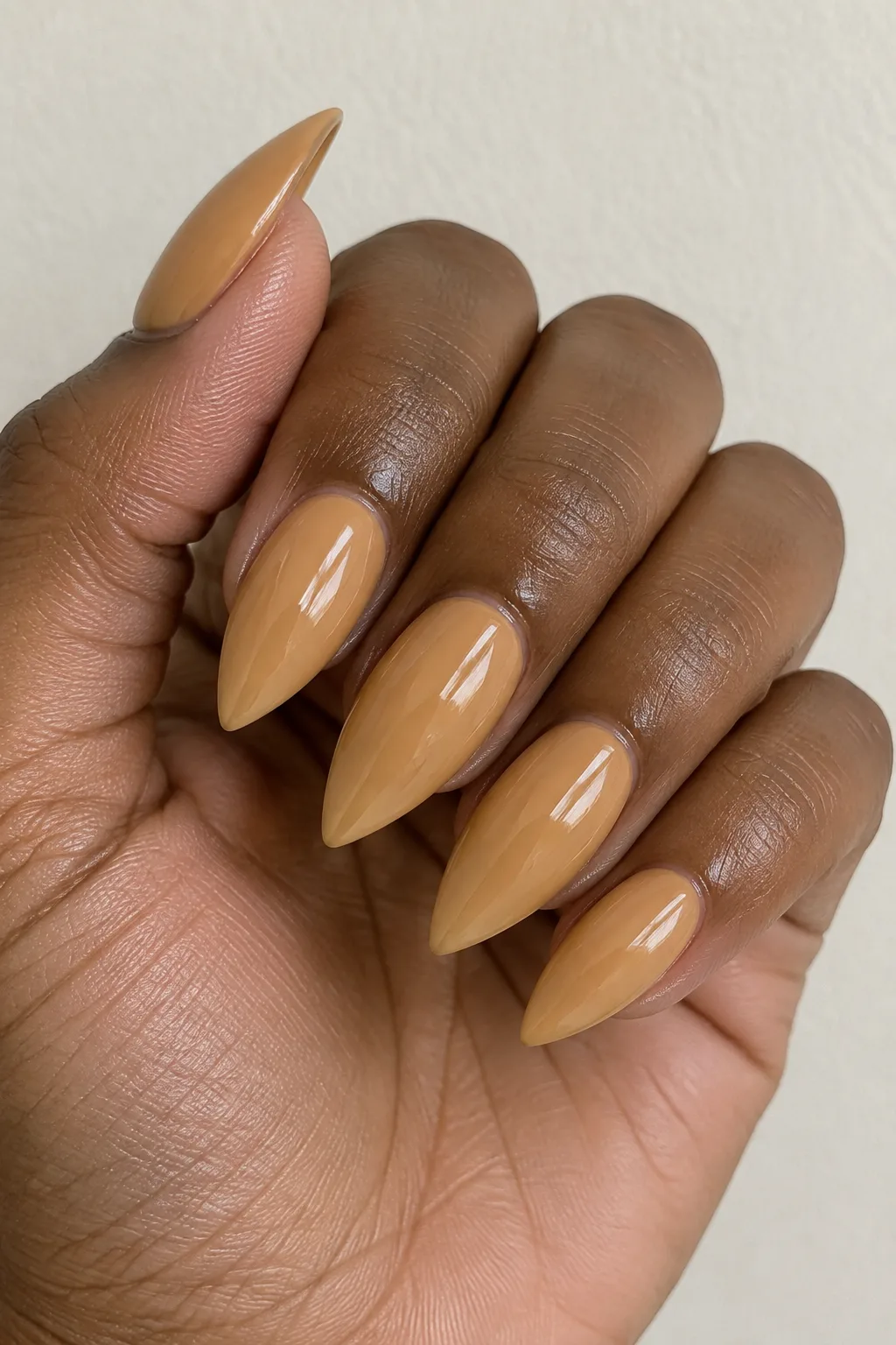 Golden honey polish on long stiletto-shaped nails with a glossy finish