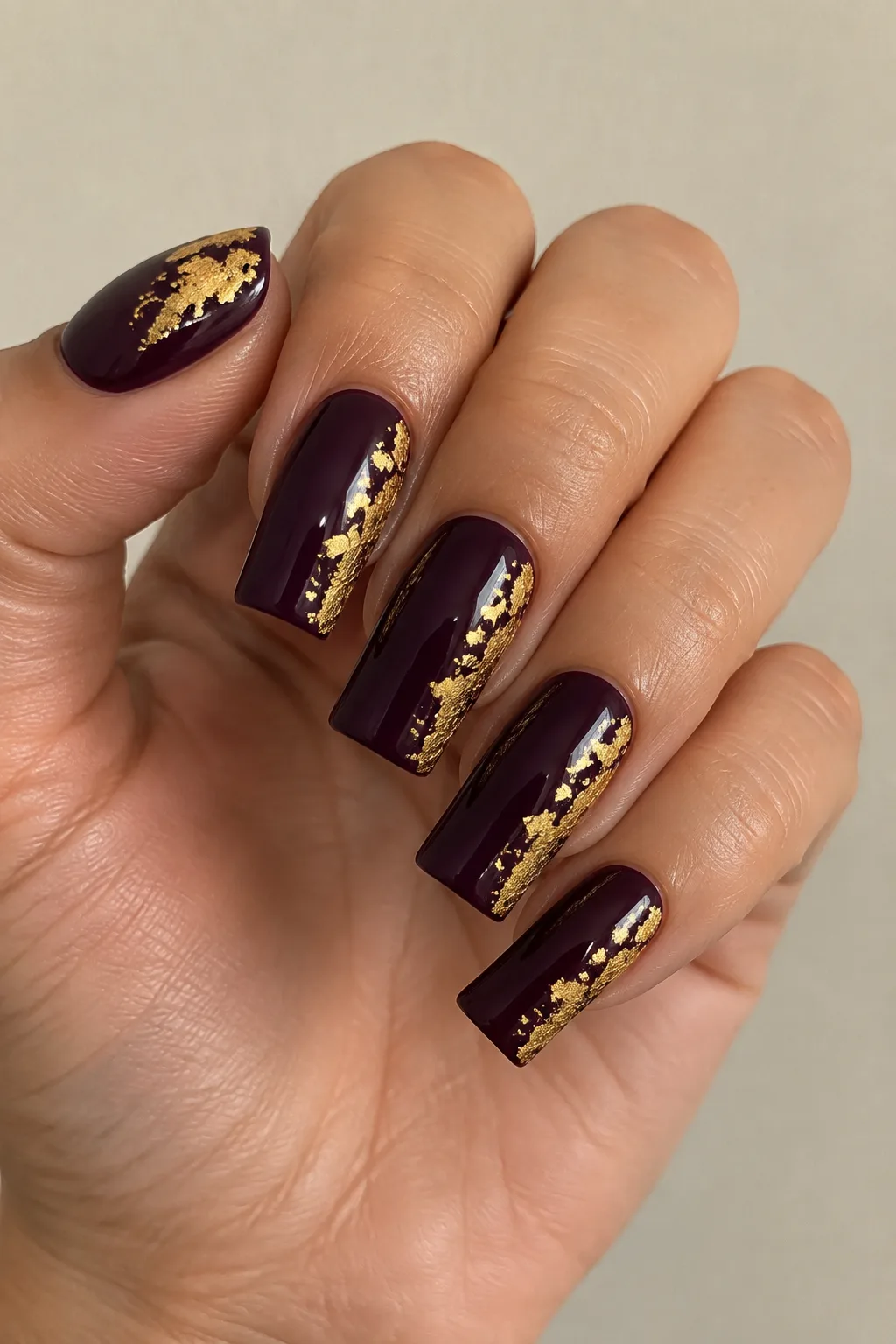 Flare shaped nails in deep plum with scattered gold leaf flakes