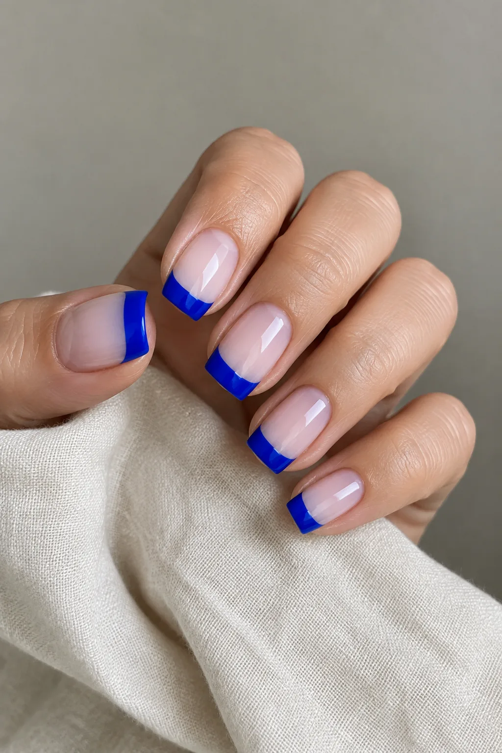 Glossy cobalt blue French tips on medium almond nails over a nude base